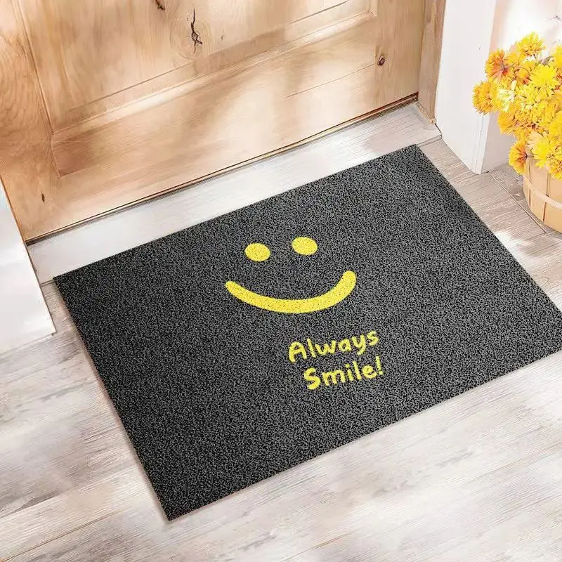 Schwarze Fußmatte mit gelbem Lächeln und Schriftzug „Always Smile!“ vor einer Holztür