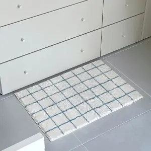 Rechteckige Badematte mit blauem Karomuster auf weißem Grund auf grauem Fliesenboden