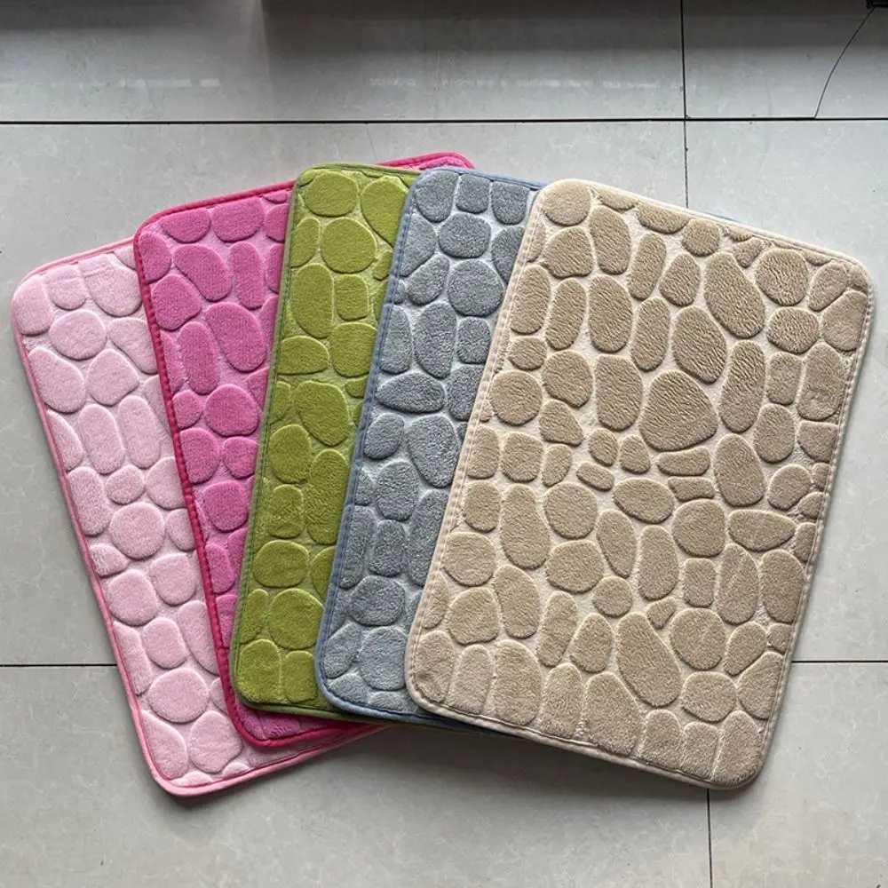 Fünf Badematten mit Kieselstein-Prägung in Rosa, Magenta, Grün, Grau und Beige auf Fliesen