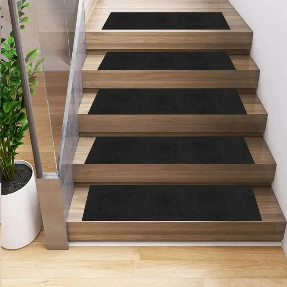 Schwarze Stufenmatten liegen auf Holzstufen einer Treppe neben einem Glasgeländer